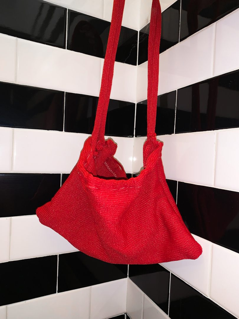 red hand-knit bag hanging in front of black and white stripes of tiles