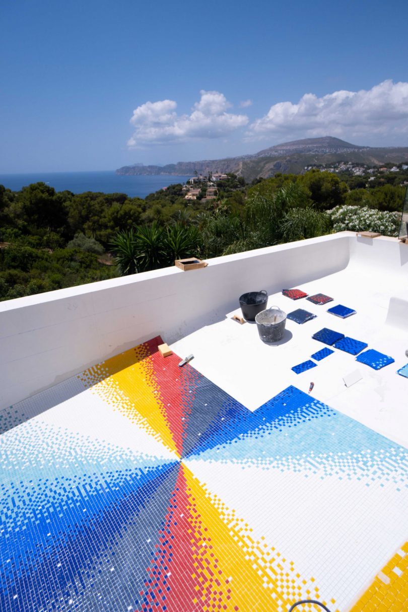 looking down into empty swimming pool with colorful mosaic tile being laid