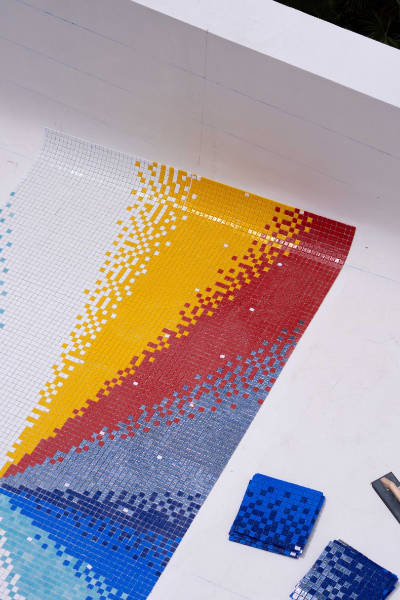 looking down into empty swimming pool with colorful mosaic tile being laid