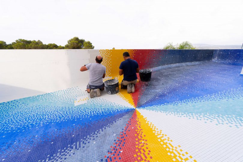 looking down into empty swimming pool with colorful mosaic tile being laid