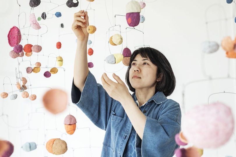 artist with art installation of suspended colored disks in white room