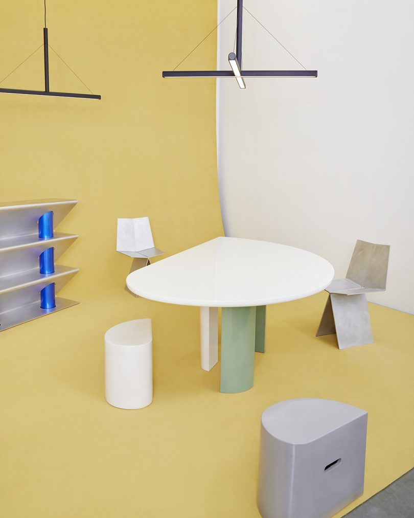 dining table, two dining chairs, two stools, table sculpture, and lighting on butter yellow background