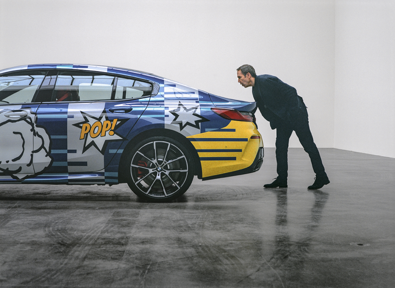 side of colorful graphic sports car with man standing behind the car leaning over to inspect something