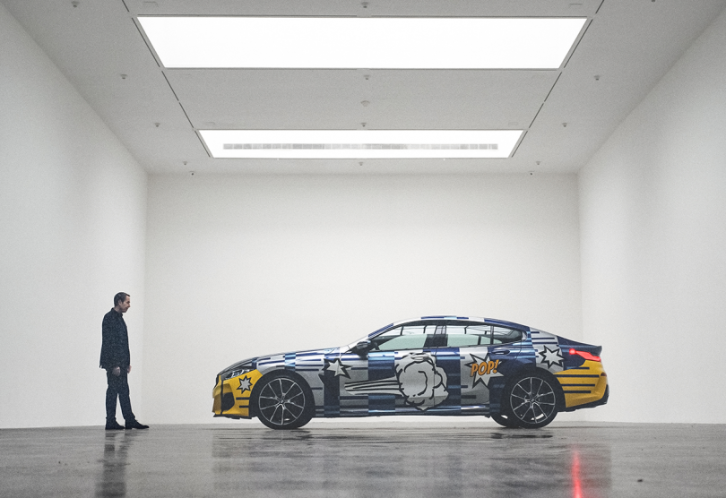 side of colorful graphic sports car with man standing in front of hood