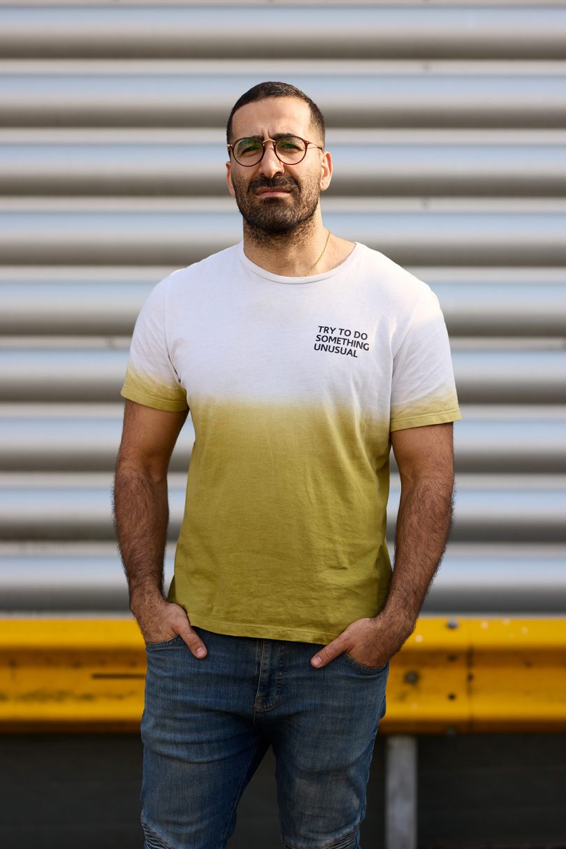 brown skinned man wearing yellow and white t-shirt, jeans, and glasses