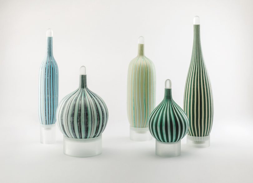 five striped murano glass vessels on a white background