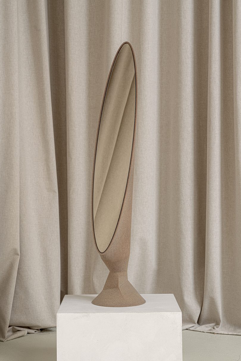 light brown oblong floor mirror on white pedestal in front of light fabric