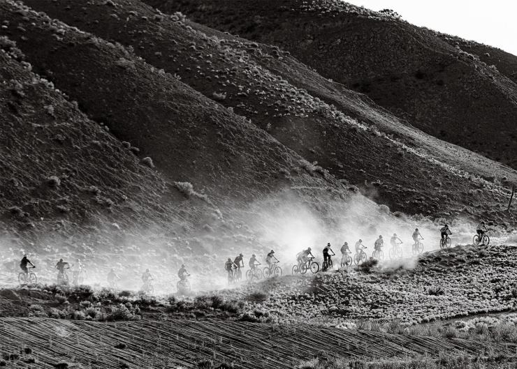 bike riders in a line riding a dirt trail in front of a mountain