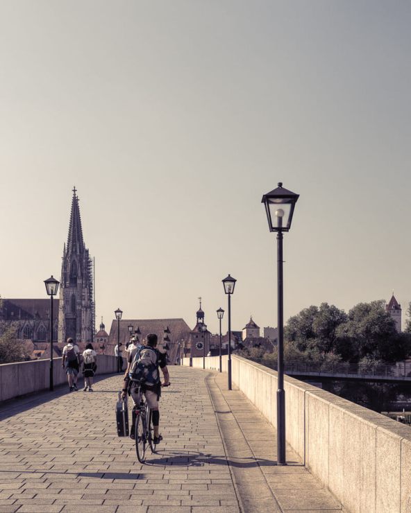 Man carrying guitar riding across Regensburg Stone Bridge